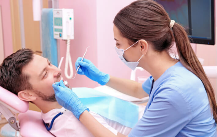 A male dental patient receiving a dental cleaning from a female dental hygienist