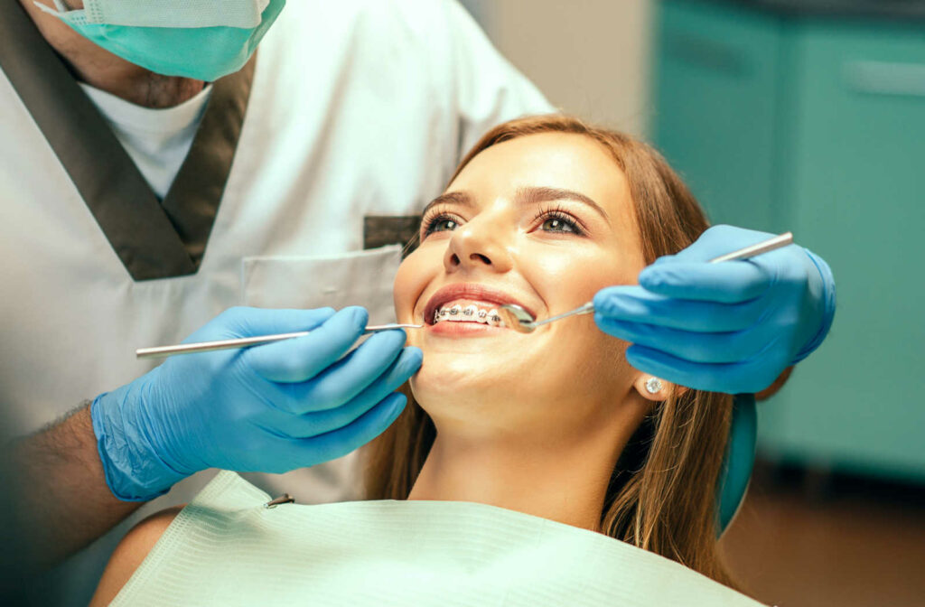 A smiling female patient has her braces examined by a dentist.