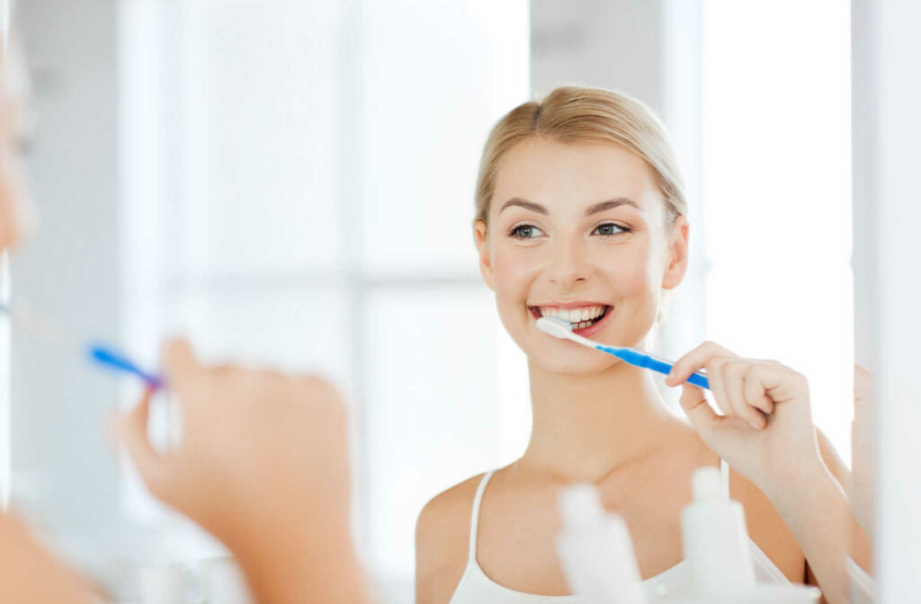 A young woman in the mirror is smiling and holding a toothbrush cleaning her teeth.
