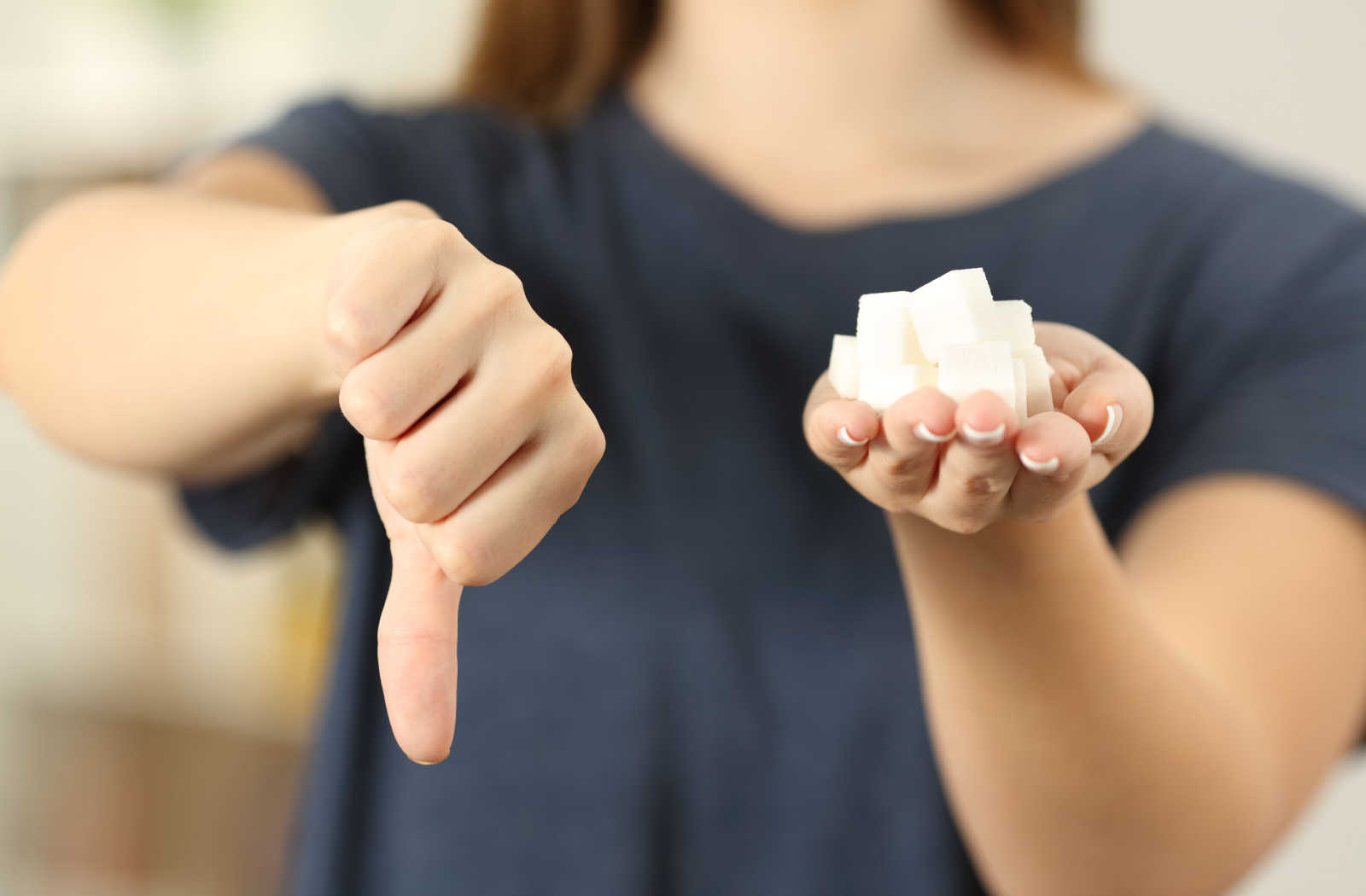 A close-up of a woman with her left hand holding sugar cubes in her palm and thumbs down on her right hand.
Eating too many sugary or acidic foods can contribute to the breakdown of your enamel, which leads to cavities and tooth decay.